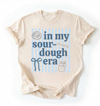 Flat lay of an ivory In my sourdough era shirt with baking icons and stripes perfect gift for sourdough lovers and home bakers on a white background