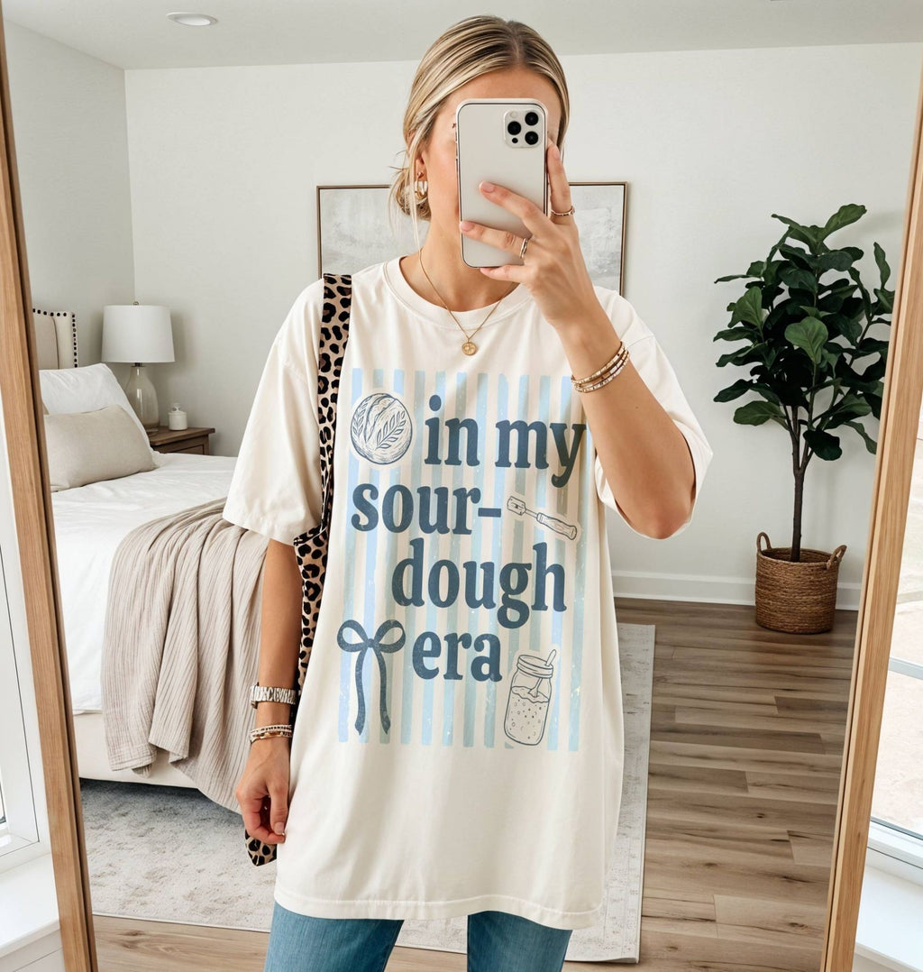 Person wearing a white t-shirt with text and graphics, standing in a bedroom.