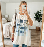 Person wearing a white t-shirt with text and graphics, standing in a bedroom.