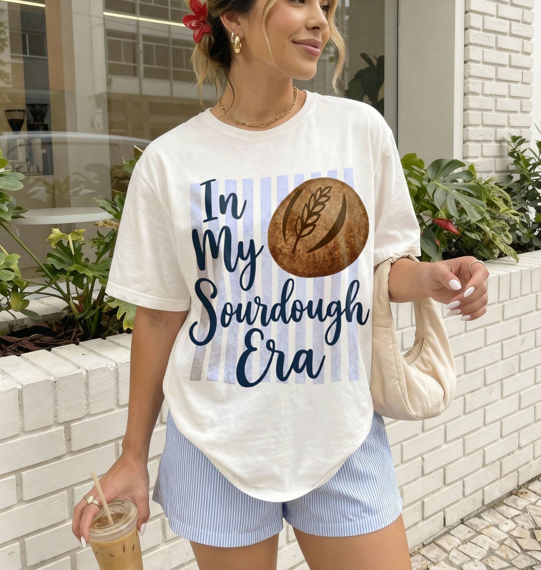 Woman wearing a t-shirt with 'In My Sourdough Era' design, holding a drink, standing outdoors.