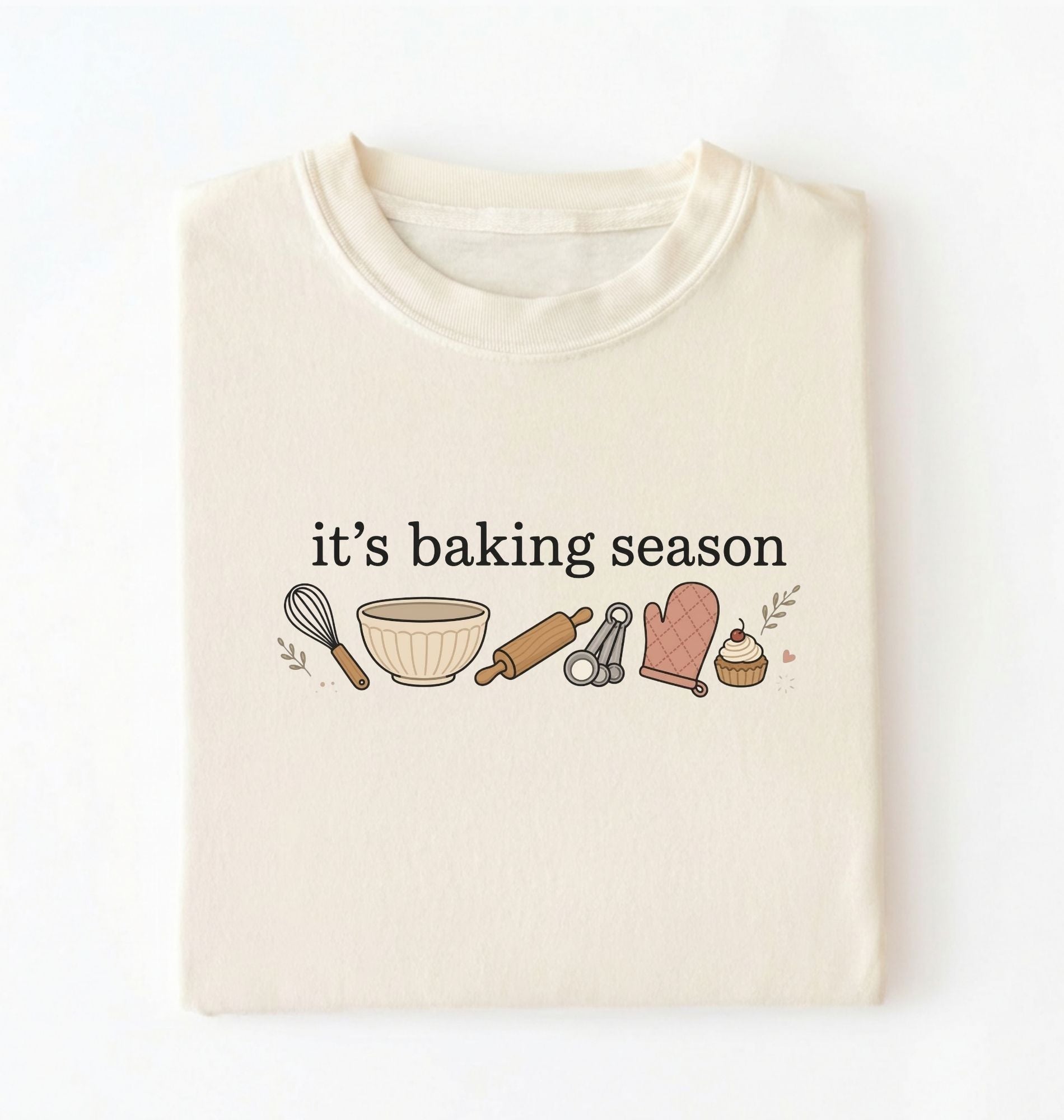 Flat lay of a ivory its baking season shirt with baking tools cupcake and oven mitt cute baker gift on a white background 
