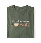 Flat lay of a green its baking season shirt with baking tools cupcake and oven mitt cute baker gift on a white background 