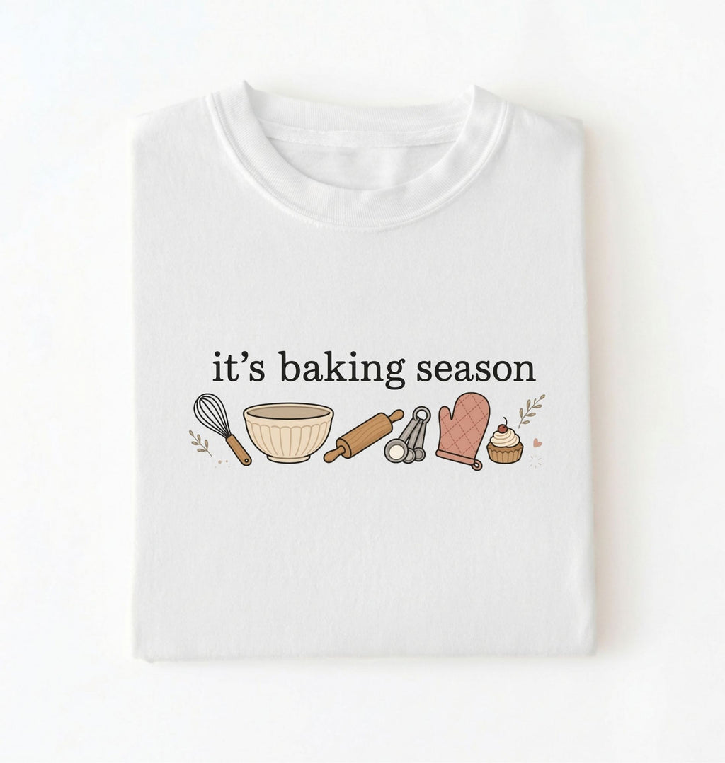 Flat lay of a white its baking season shirt with baking tools cupcake and oven mitt cute baker gift on a white background 