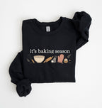 Flat lay of a black It's Baking Season graphic sweatshirt featuring baking tools and cupcake design on a white background 