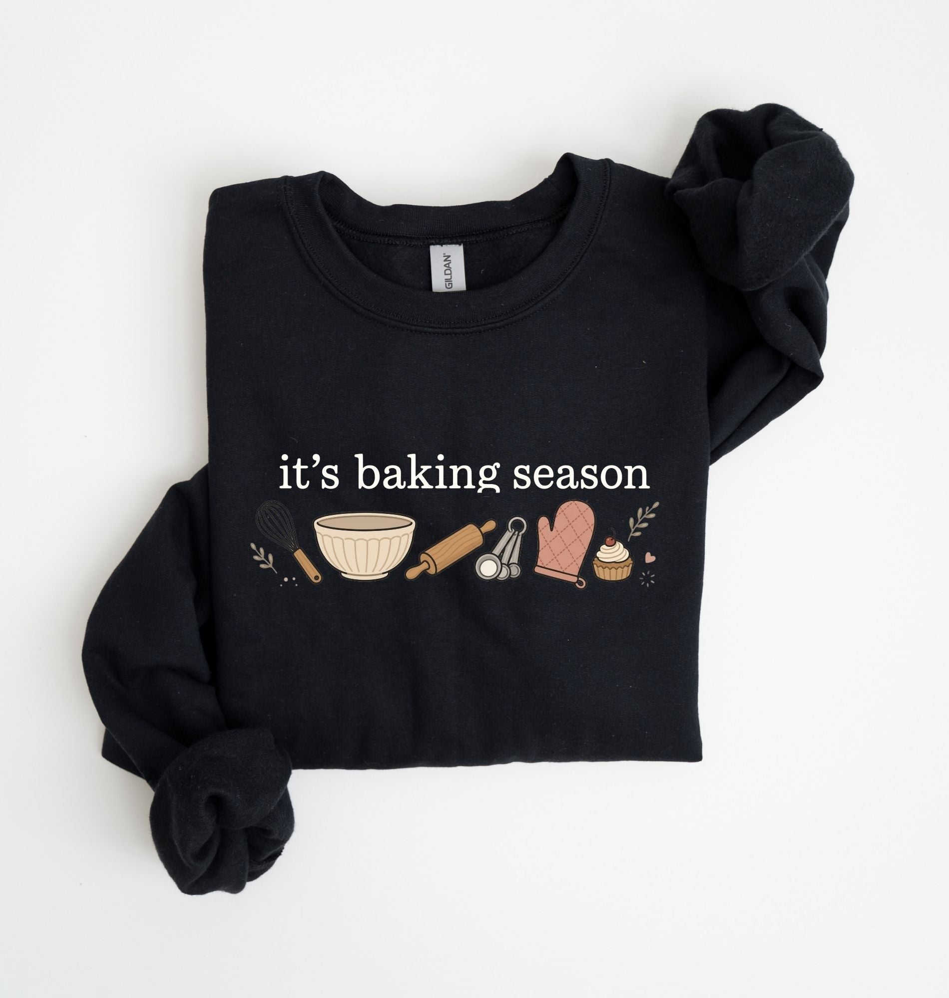 Flat lay of a black It's Baking Season graphic sweatshirt featuring baking tools and cupcake design on a white background 
