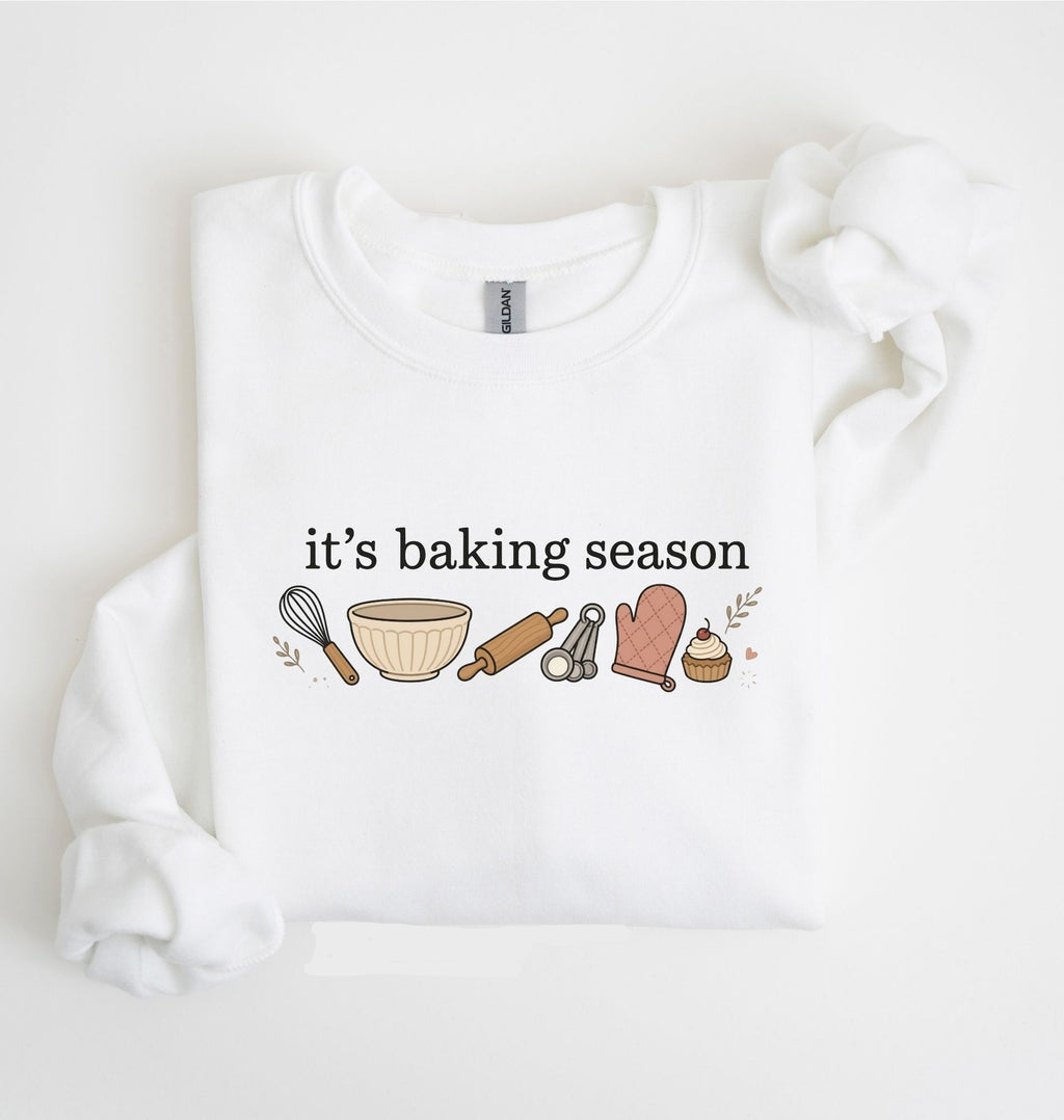 Flat lay of a white It's Baking Season graphic sweatshirt featuring baking tools and cupcake design on a white background 