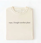 Flat lay ivory t-shirt with 'oops, I bought another plant' with humorous text on a white background