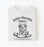 Flat lay of a white Kitty Biscuits Bakery shirt featuring a baking kitten and dough on cream t-shirt on  a white background 