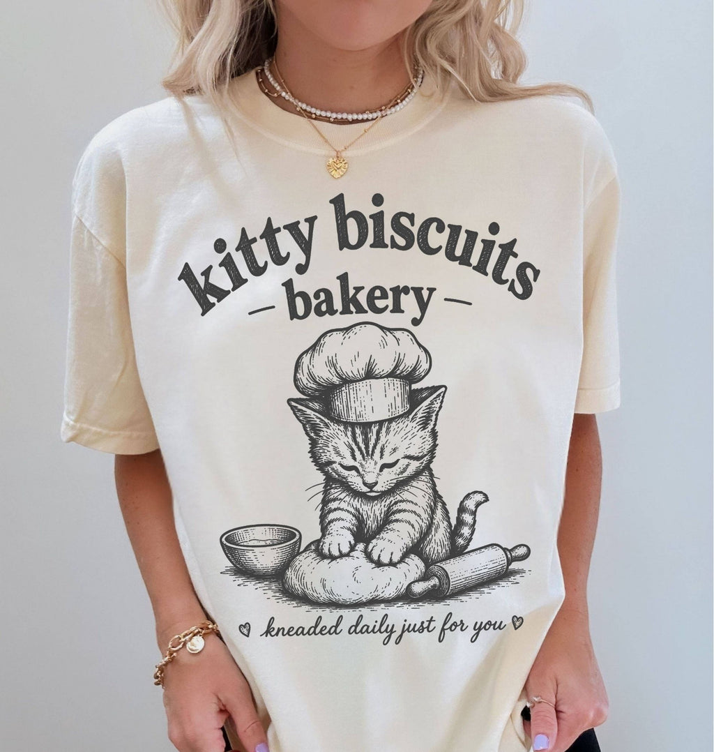 Person wearing a white t-shirt with a cat graphic and 'kitty biscuits bakery' text.
