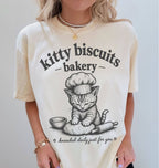 Person wearing a white t-shirt with a cat graphic and 'kitty biscuits bakery' text.