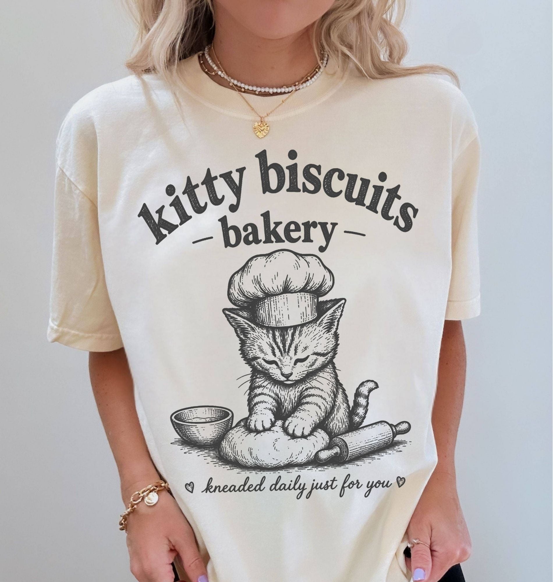 Person wearing a white t-shirt with a cat graphic and 'kitty biscuits bakery' text.