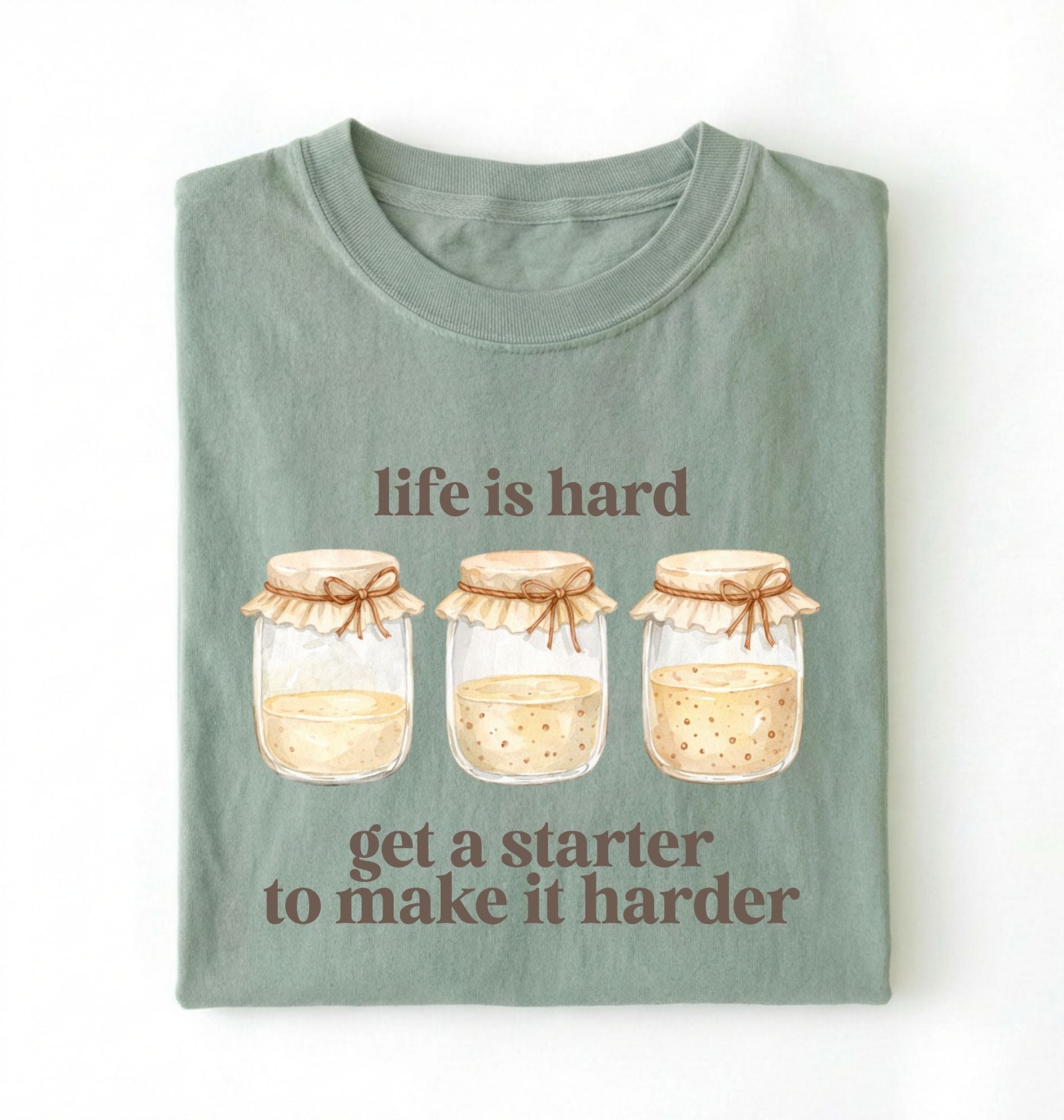 Flat lay of a bay Funny Life Is Hard Get a Starter sourdough shirt with sourdough starter jars on brown t-shirt on a white background 