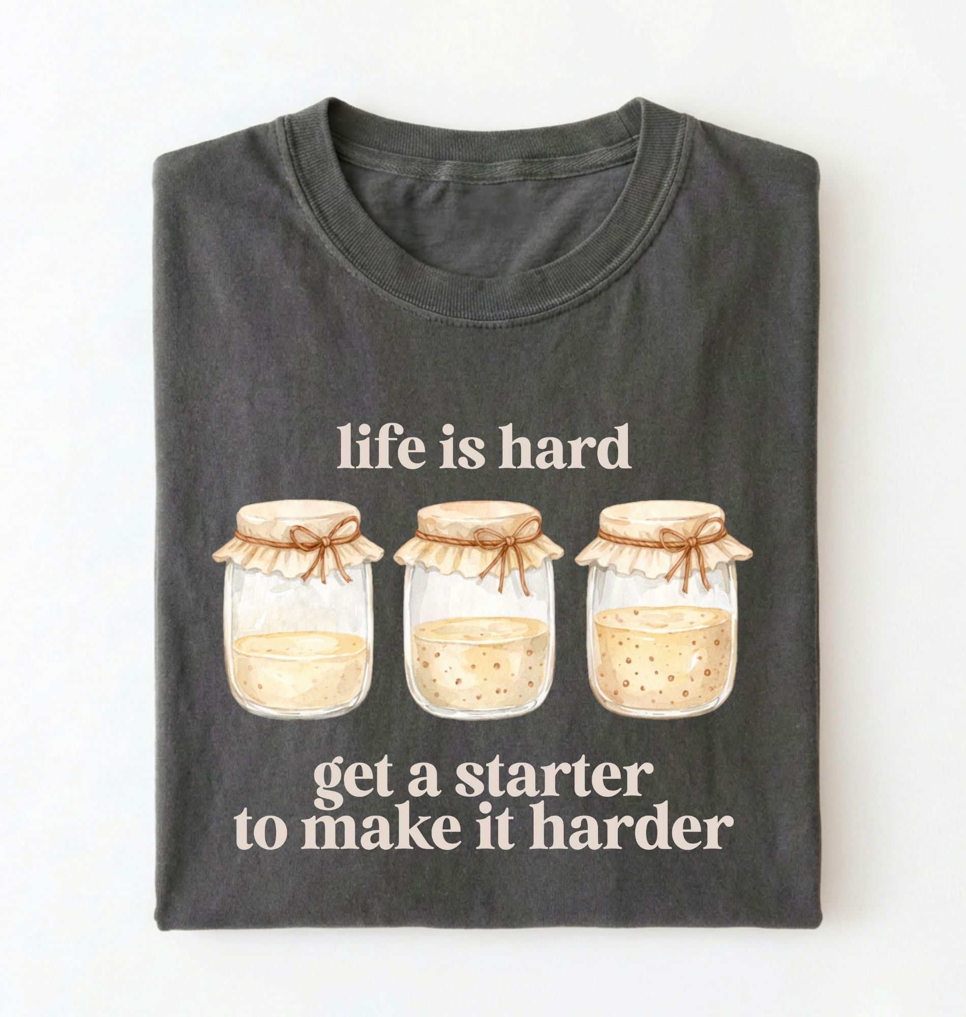 Flat lay of a pepper Funny Life Is Hard Get a Starter sourdough shirt with sourdough starter jars on brown t-shirt on a white background 