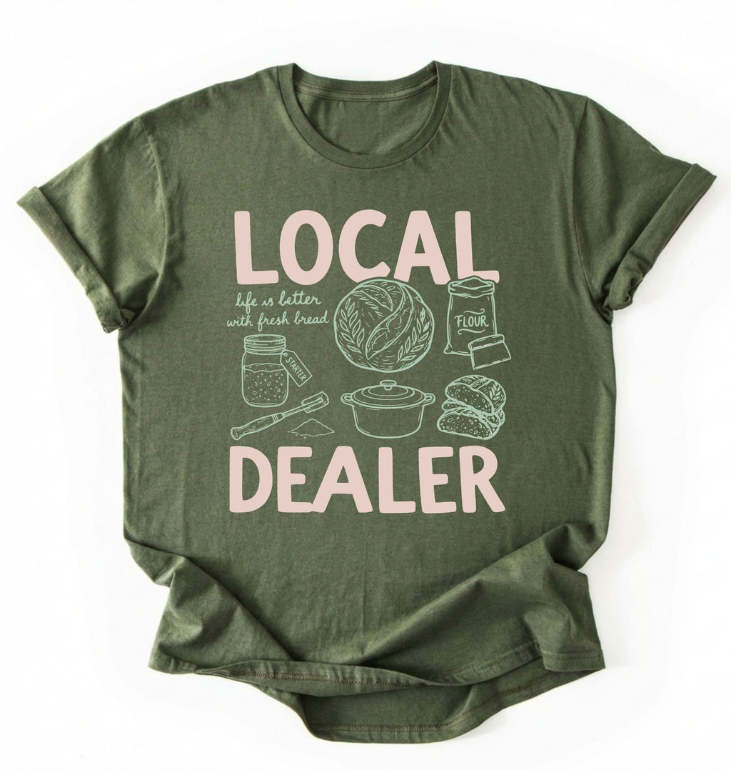 Flat lay of a Moss_MilitaryGreen Funny local dealer bread shirt with baking tools and sourdough theme perfect gift for bakers and bread lovers on a white background 