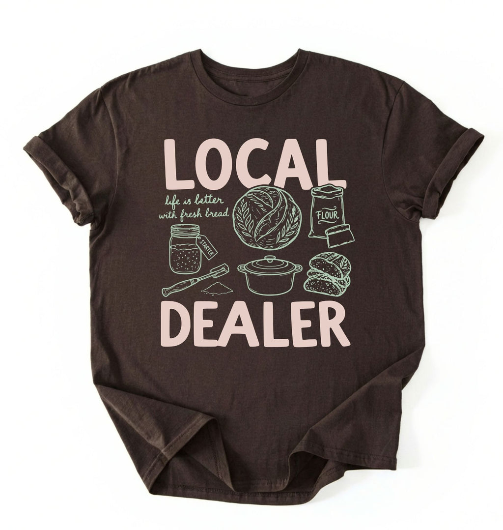 Flat lay of a dark chocolate Funny local dealer bread shirt with baking tools and sourdough theme perfect gift for bakers and bread lovers on a white background 