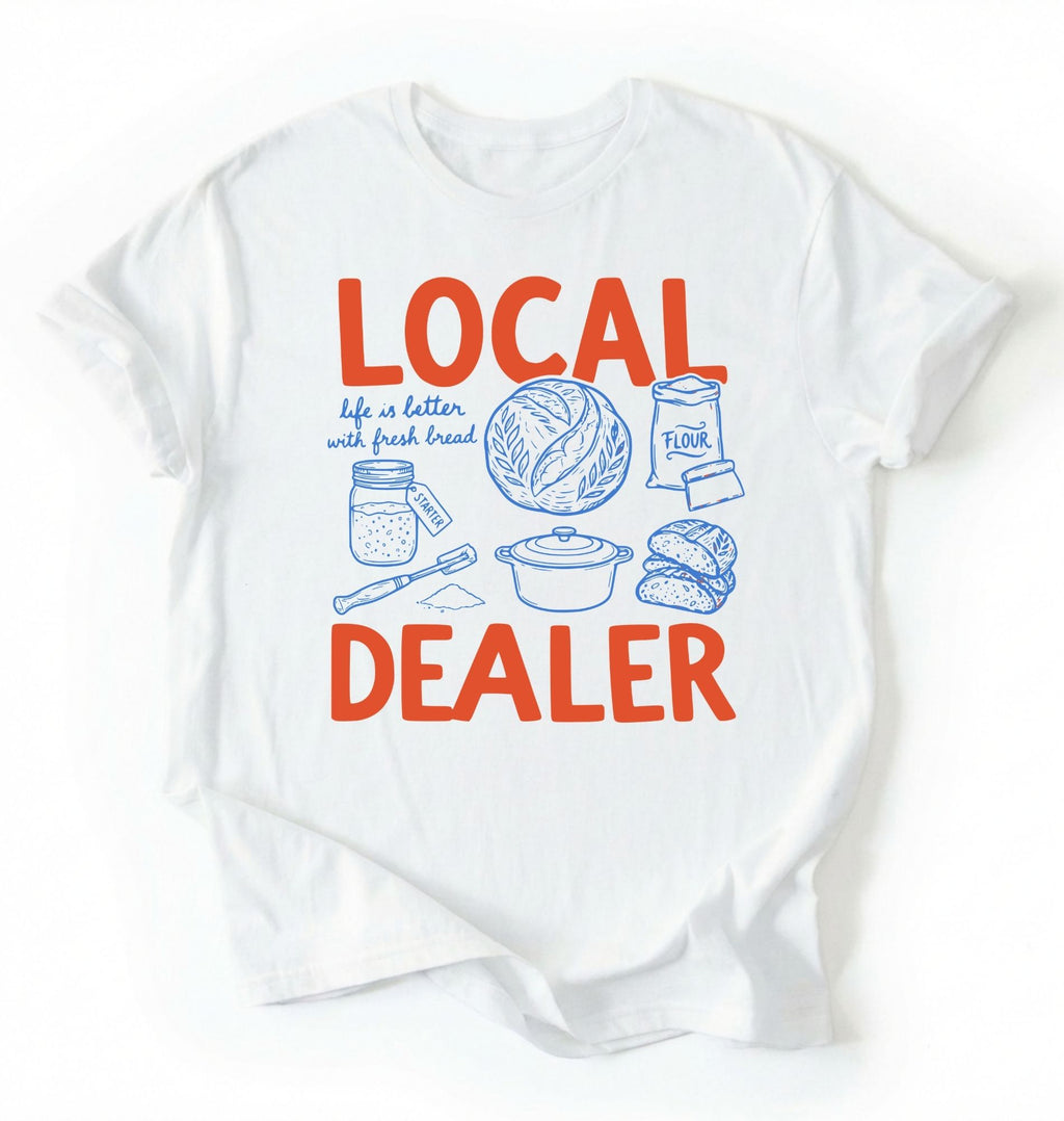 Flat lay of a white Funny local dealer bread shirt with baking tools and sourdough theme perfect gift for bakers and bread lovers on a white background 