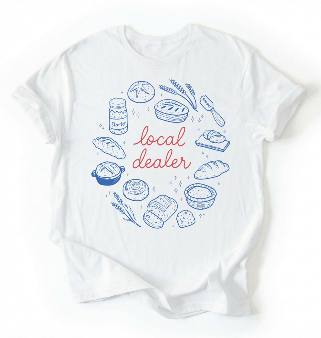 Flat lay of a white local dealer sourdough shirt with bread starter and baking illustrations funny baker gift white t-shirt on a white background