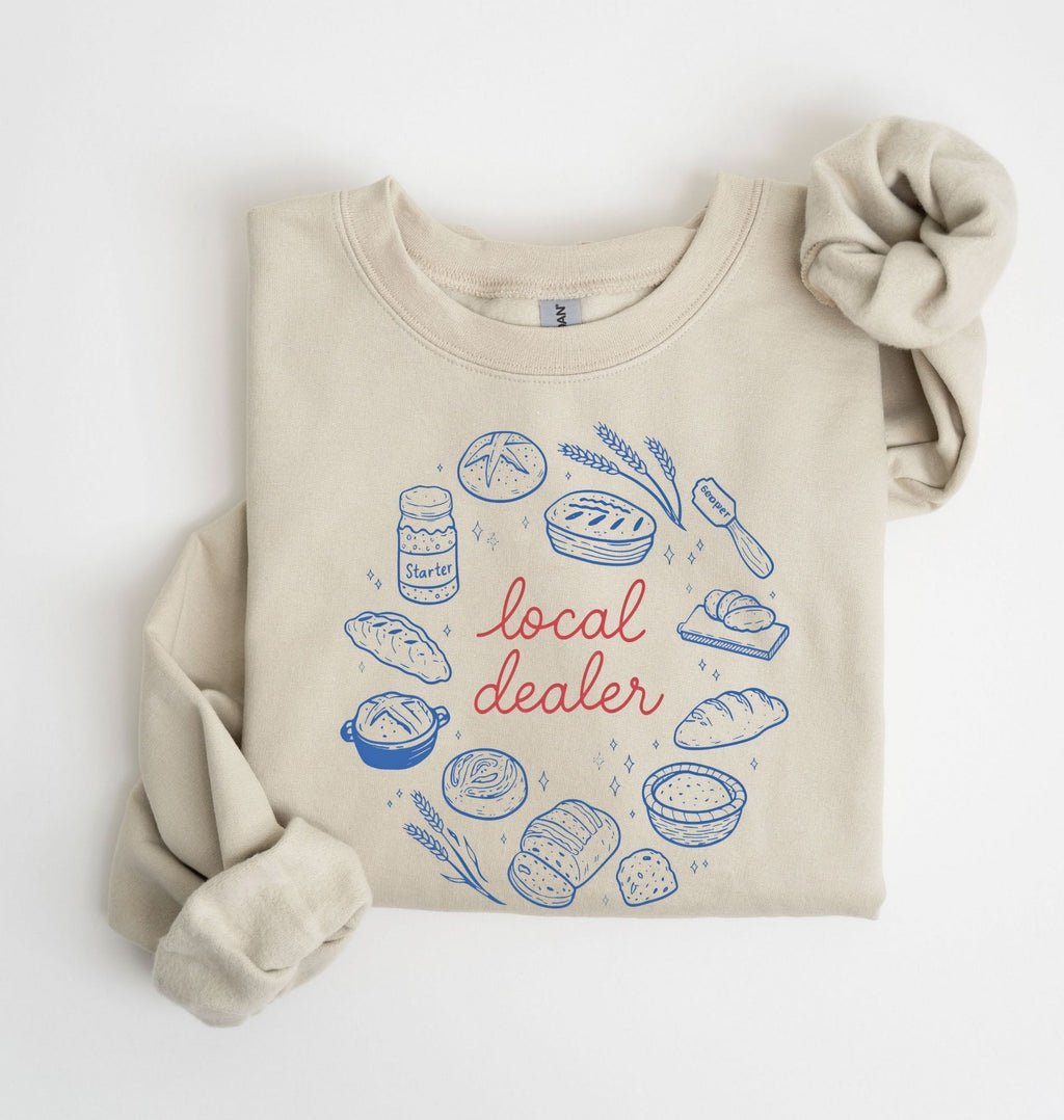 Flat lay of a sand Bakery themed crewneck featuring bread and sourdough starter graphics on a white background 