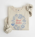Flat lay of a sand Bakery themed crewneck featuring bread and sourdough starter graphics on a white background 