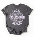 Flat lay of a charcoal local sourdough dealer shirt brown funny baking t shirt bread lover gift bakery humor on a white background 