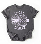 Flat lay of a charcoal local sourdough dealer shirt brown funny baking t shirt bread lover gift bakery humor on a white background 