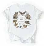 Flat lay of a white Nature inspired animal lover tee featuring raccoon, bat, frog, and opossum on a white background