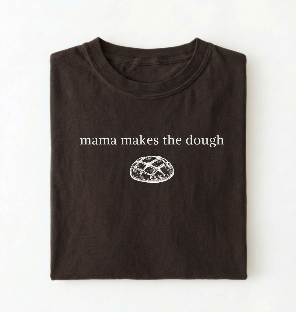 Flat lay of a darkchocolate Funny Mama Makes The Dough shirt with bread graphic on brown tee on a white background