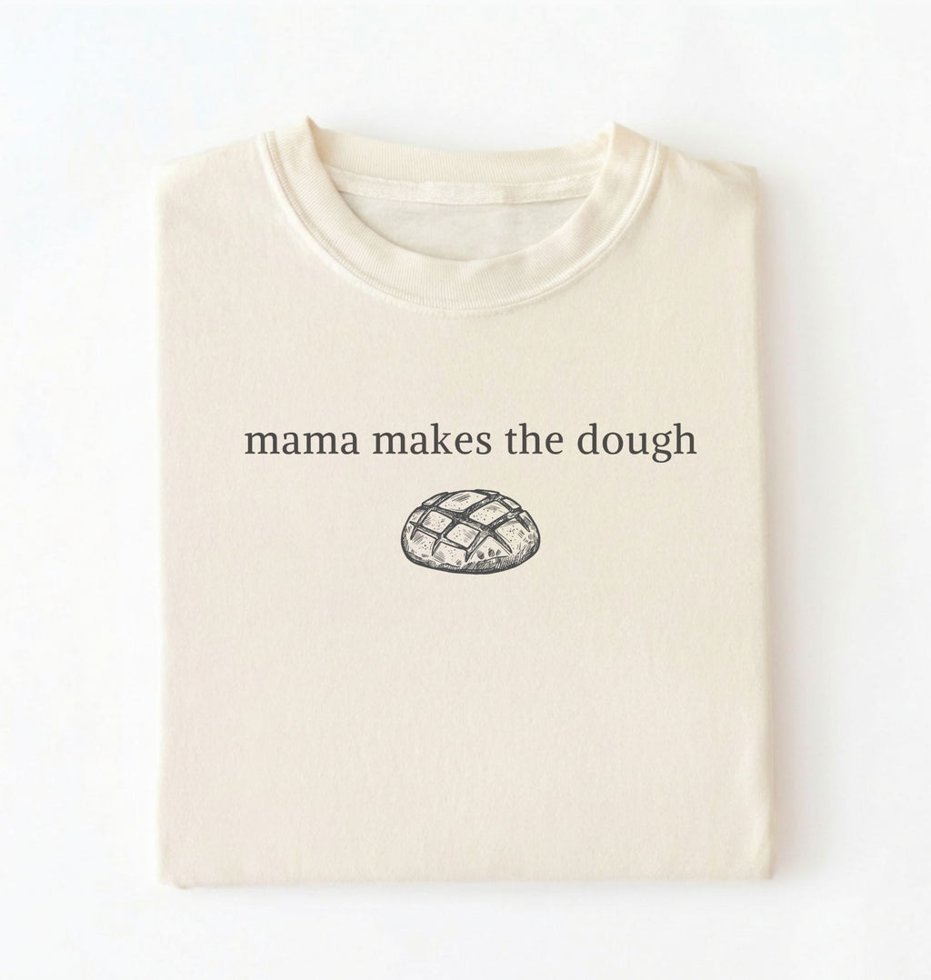 Flat lay of a ivory Funny Mama Makes The Dough shirt with bread graphic on brown tee on a white background