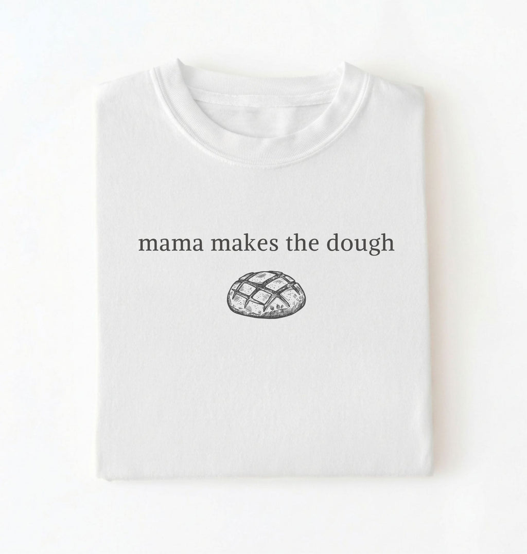 Flat lay of a white Funny Mama Makes The Dough shirt with bread graphic on brown tee on a white background