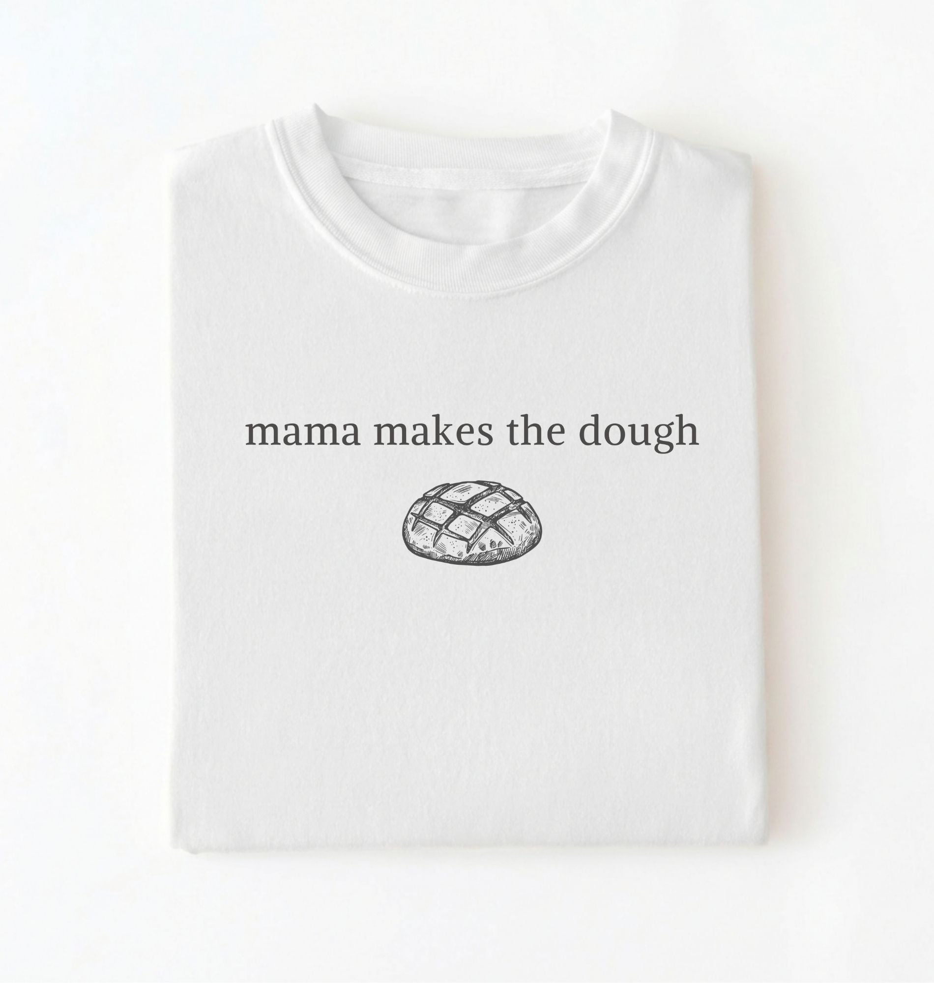 Flat lay of a white Funny Mama Makes The Dough shirt with bread graphic on brown tee on a white background
