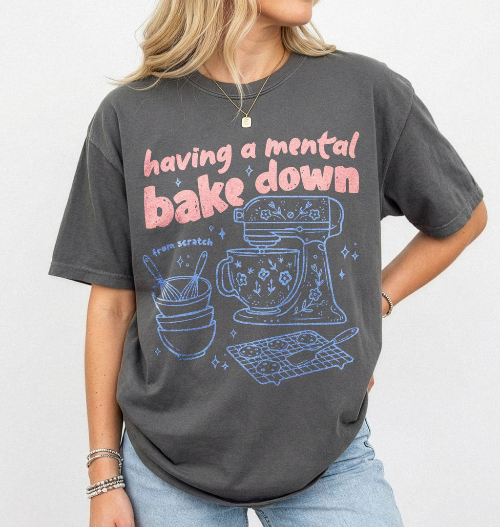 Person wearing a dark gray t-shirt with a graphic and text 'having a mental bake down' on a plain background