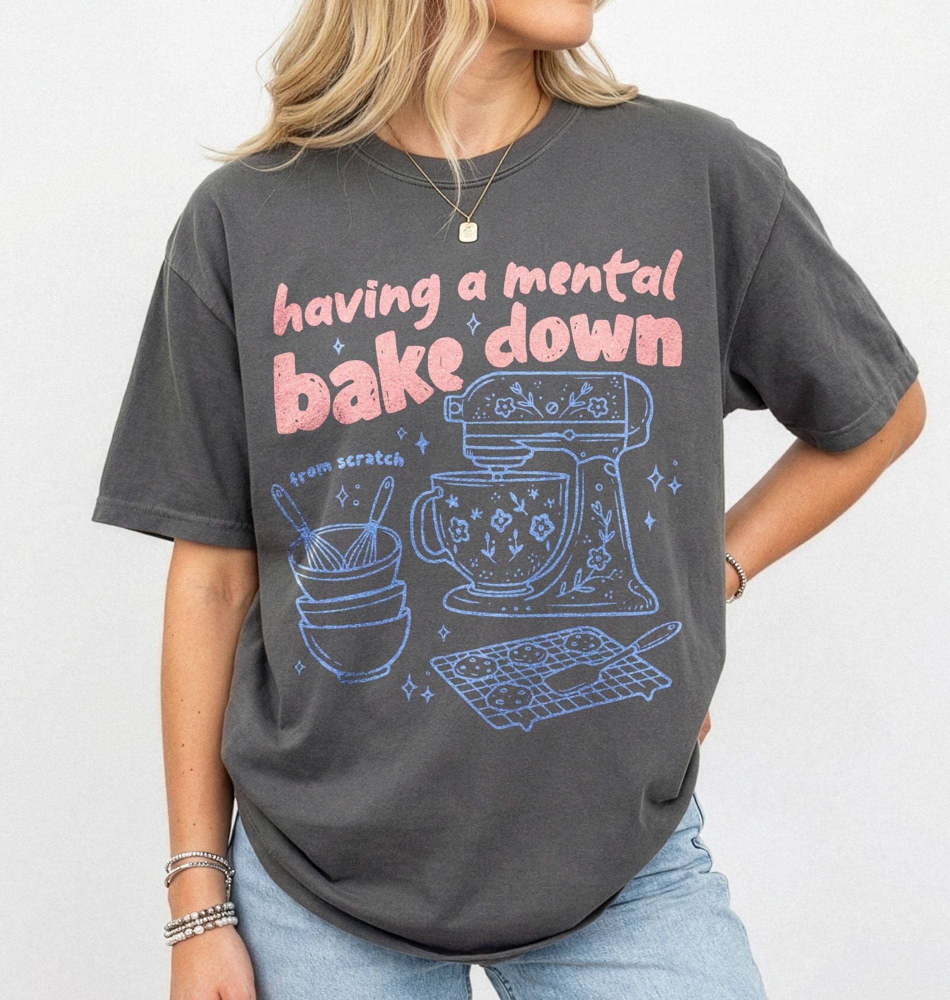 Person wearing a dark gray t-shirt with a graphic and text 'having a mental bake down' on a plain background