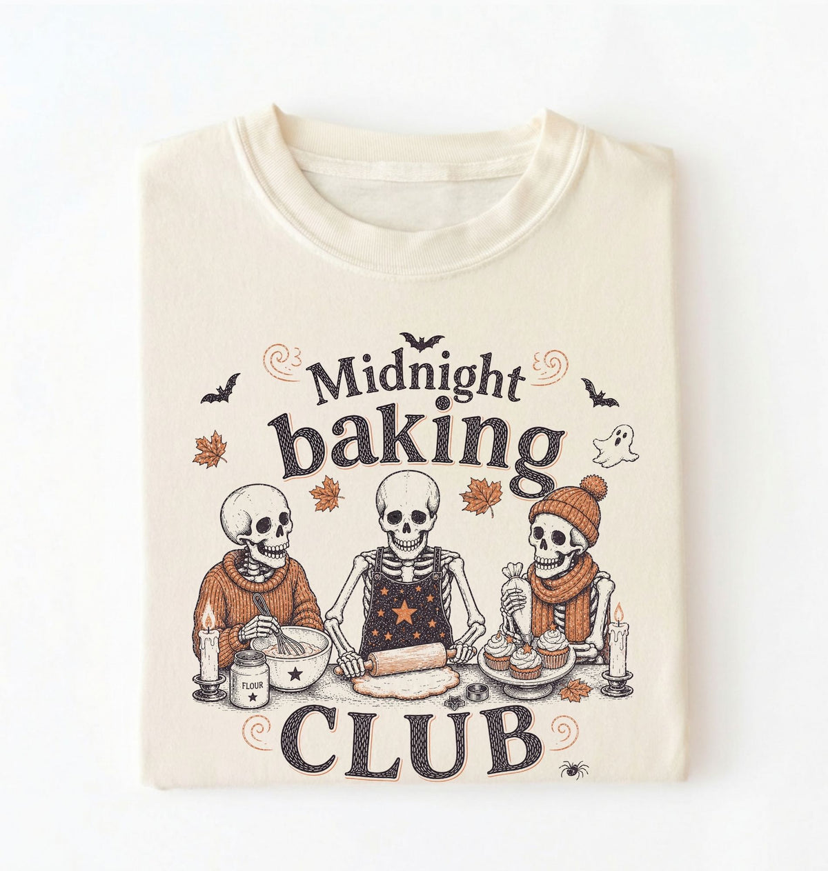 A folded cream-colored t-shirt with a graphic print of three baking skeletons and the text 'Midnight baking CLUB'.