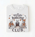 A white short-sleeve t-shirt with a Halloween-themed graphic print that reads 'Midnight baking CLUB' featuring three cartoon skeletons baking together.