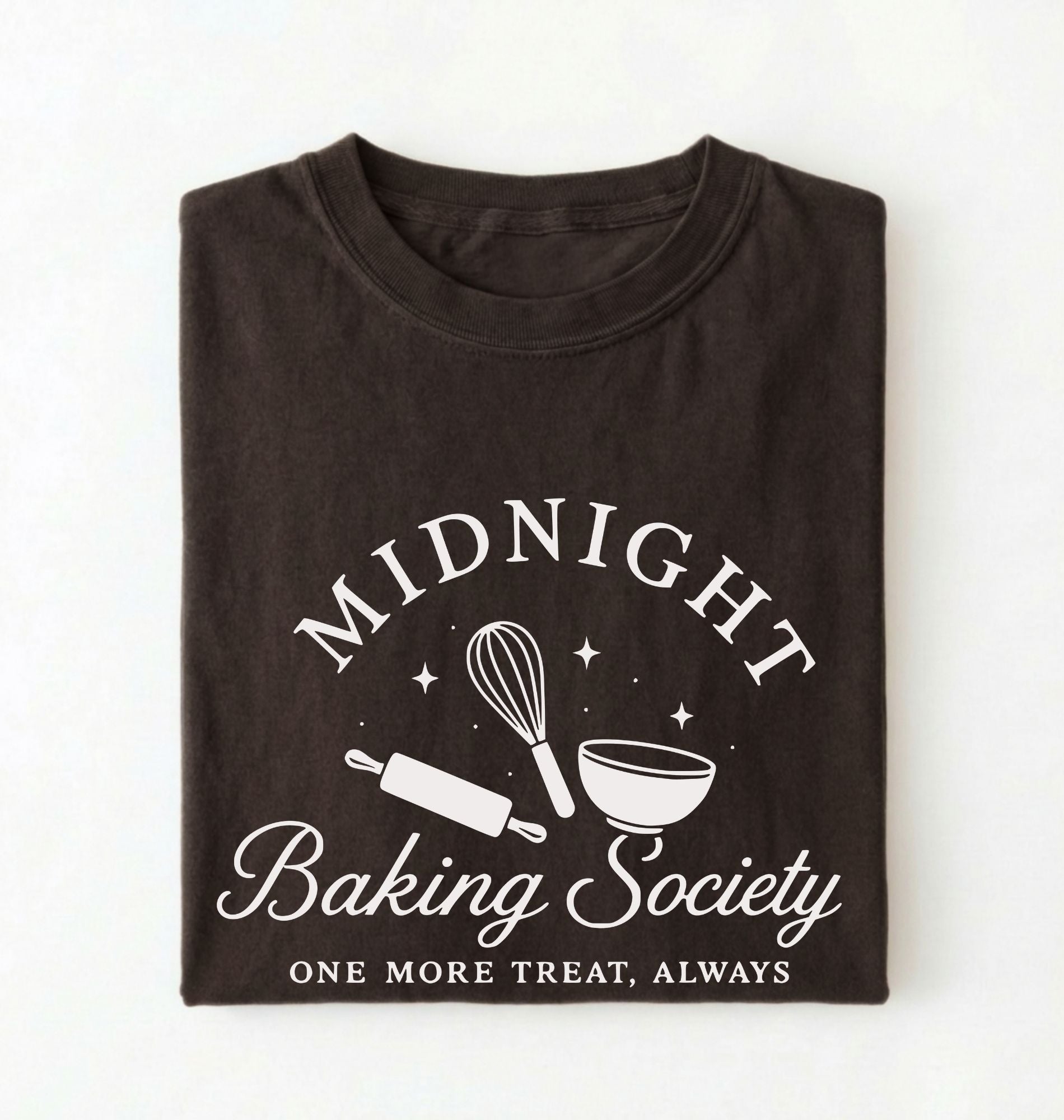 A folded dark brown t-shirt with a white graphic print that reads 'MIDNIGHT Baking Society' and 'ONE MORE TREAT, ALWAYS' with baking utensil illustrations, shown on a plain white background.