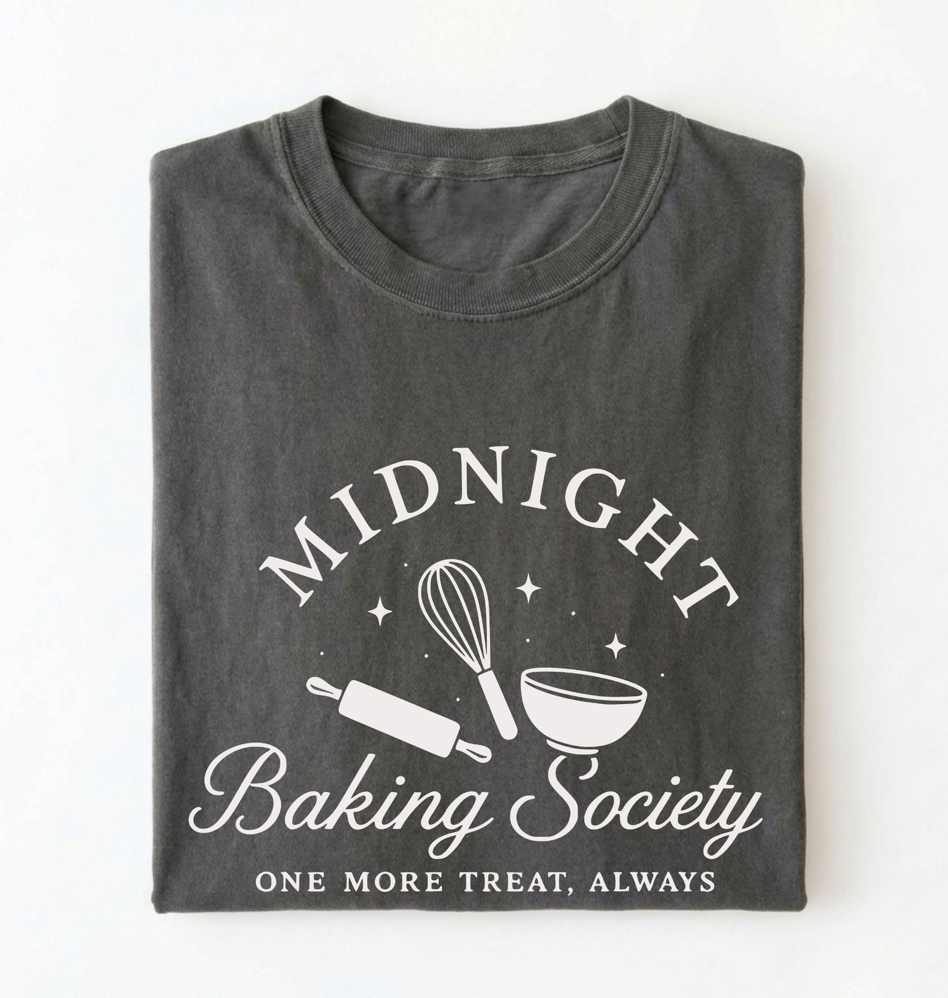 A dark gray folded t-shirt with a white graphic print that reads 'MIDNIGHT Baking Society' and 'ONE MORE TREAT, ALWAYS' with baking tools like a whisk, rolling pin, and bowl.