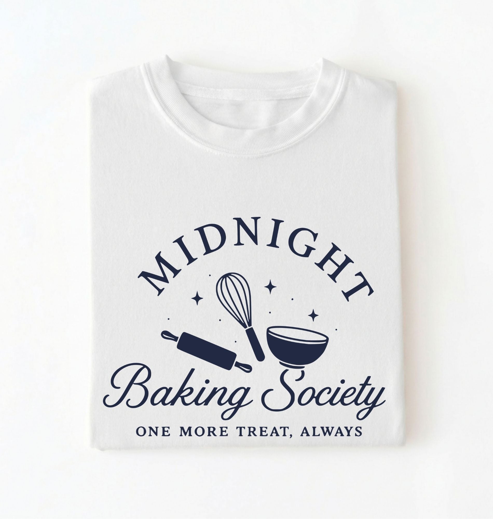 A folded white t-shirt with a navy blue graphic that reads 'MIDNIGHT Baking Society' and 'ONE MORE TREAT, ALWAYS' with illustrations of a whisk, rolling pin, and bowl.