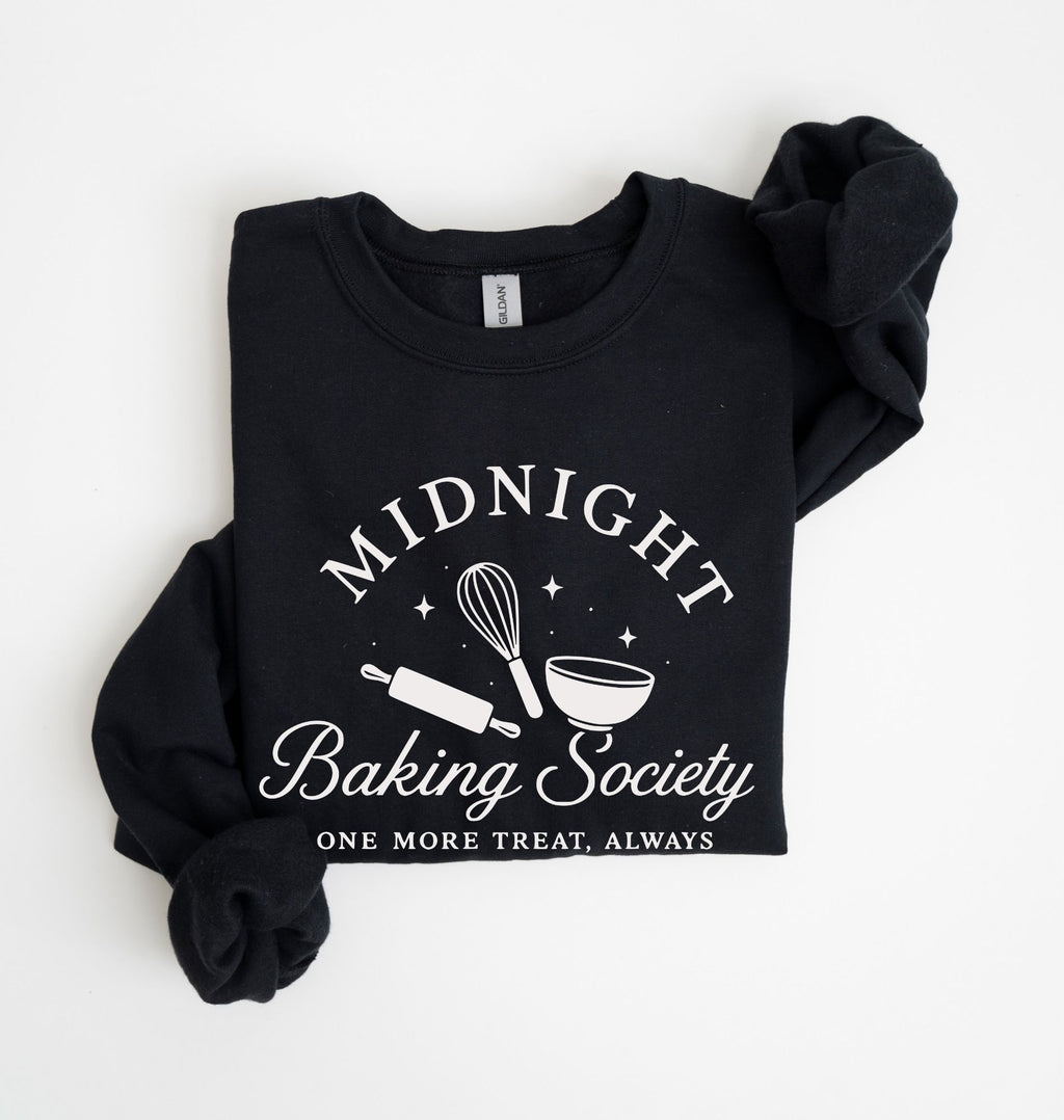 A black long-sleeve sweatshirt with rolled cuffs, featuring a white graphic print that reads 'MIDNIGHT Baking Society' and 'ONE MORE TREAT, ALWAYS' with baking tools like a whisk, rolling pin, and bowl. Photographed flat on a white background.