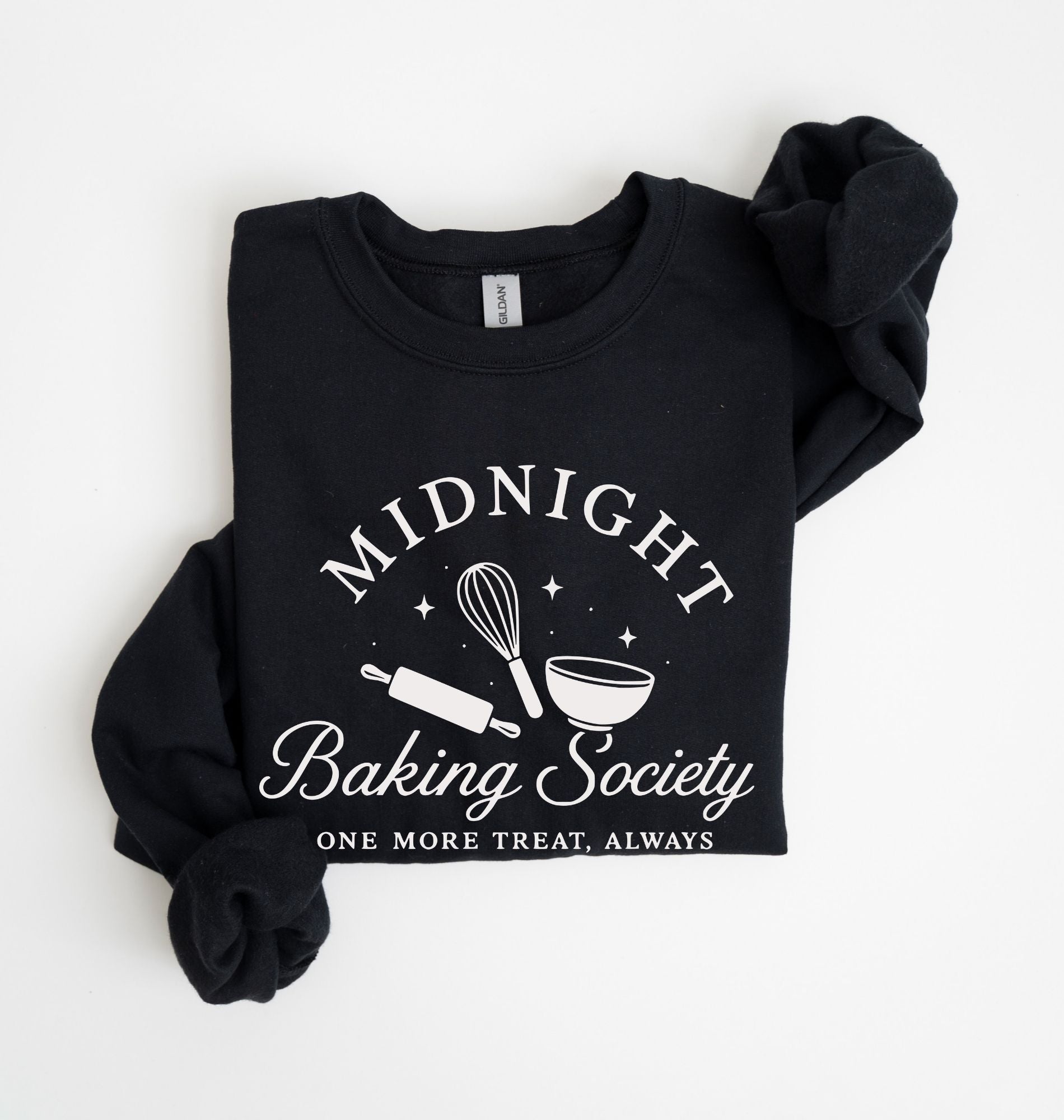 A black long-sleeve sweatshirt with rolled cuffs, featuring a white graphic print that reads 'MIDNIGHT Baking Society' and 'ONE MORE TREAT, ALWAYS' with baking tools like a whisk, rolling pin, and bowl. Photographed flat on a white background.