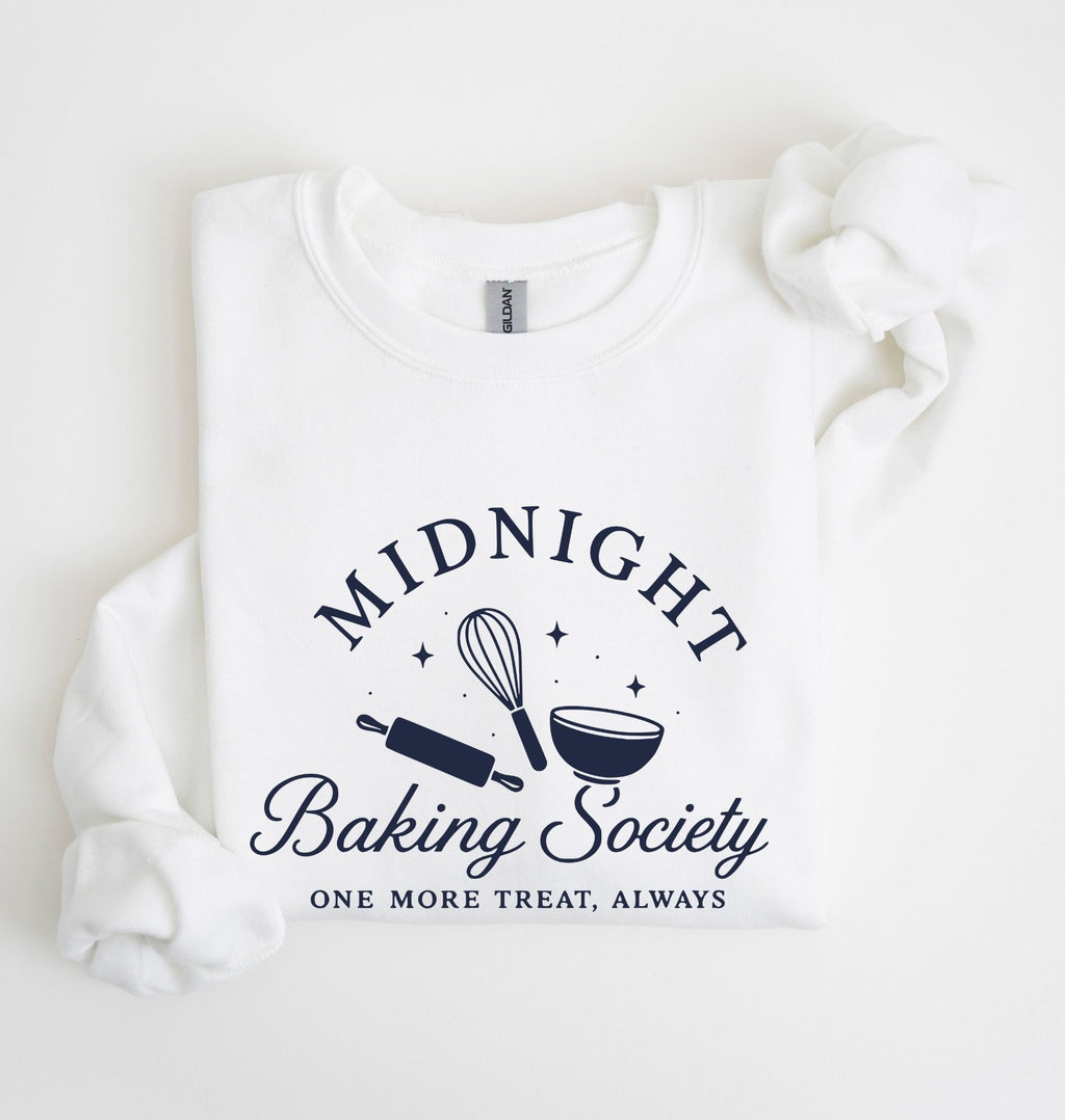 A folded white sweatshirt on a white background, featuring a navy blue graphic that reads 'MIDNIGHT Baking Society' with a whisk, rolling pin, and bowl illustration, and the phrase 'ONE MORE TREAT, ALWAYS' below.