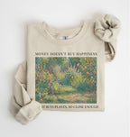 Flat lay of a sand crewneck sweatshirt on a white background, featuring an impressionist floral garden artwork and black text reading “Money doesn’t buy happiness, but it buys plants, so close enough.