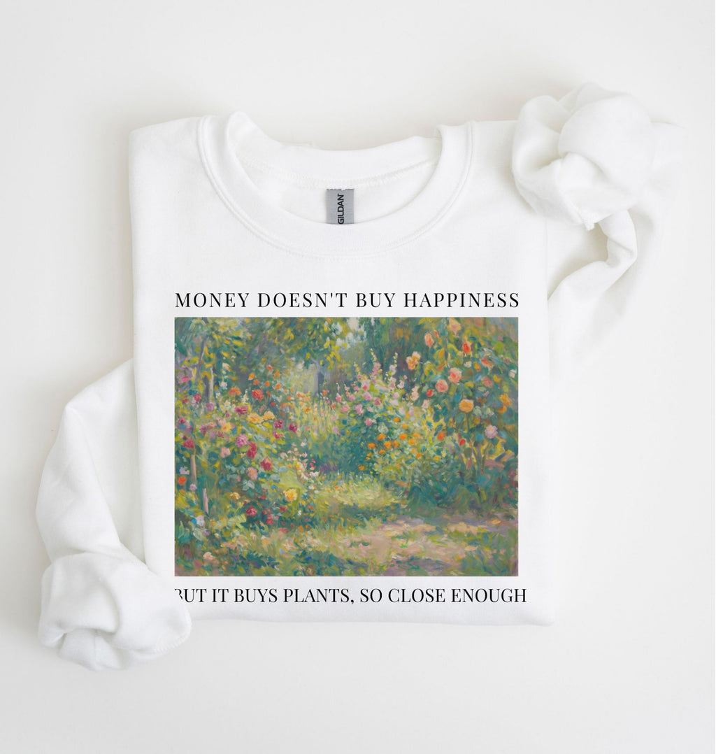 Flat lay of a white crewneck sweatshirt on a white background, featuring an impressionist floral garden artwork and black text reading “Money doesn’t buy happiness, but it buys plants, so close enough.
