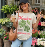 Girl holding an iced coffee infront of a plant store with an ivory tshirt that says "monstera deliciosa" with a vintage style monstera graphic