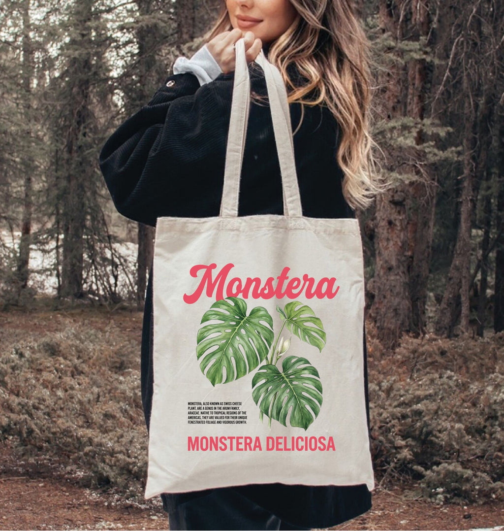 Person holding a tote bag with 'Monstera' design in a forest setting