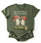 Flat lay of a Moss_Military_Green t-shirt with two dancing mushrooms and the phrase take more chances dance more dances, whimsical cottagecore gift tee on a white background 