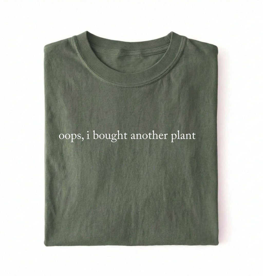 Flat lay green t-shirt with 'oops, I bought another plant' with humorous text on a white background