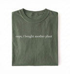 Flat lay green t-shirt with 'oops, I bought another plant' with humorous text on a white background