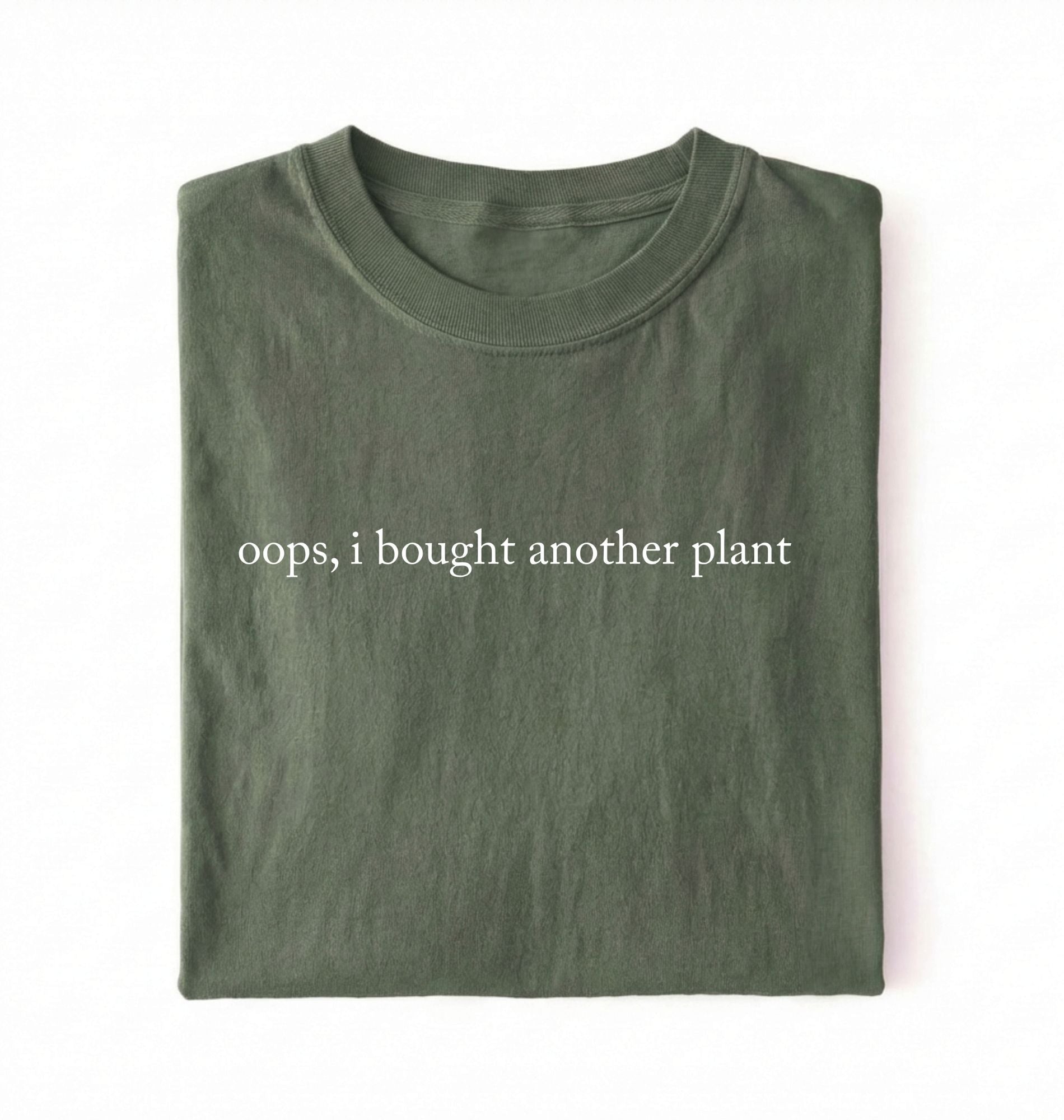 Flat lay green t-shirt with 'oops, I bought another plant' with humorous text on a white background