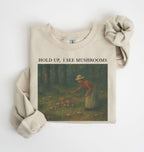 Flat lay of an sand Cottagecore mushroom sweatshirt Hold Up I See Mushrooms design beige crewneck for nature lovers on a white background