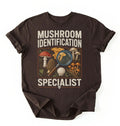 Flat lay of a brown mushroom identification specialist shirt black funny foraging t shirt fungi lover gift nature hiking design on a white background 